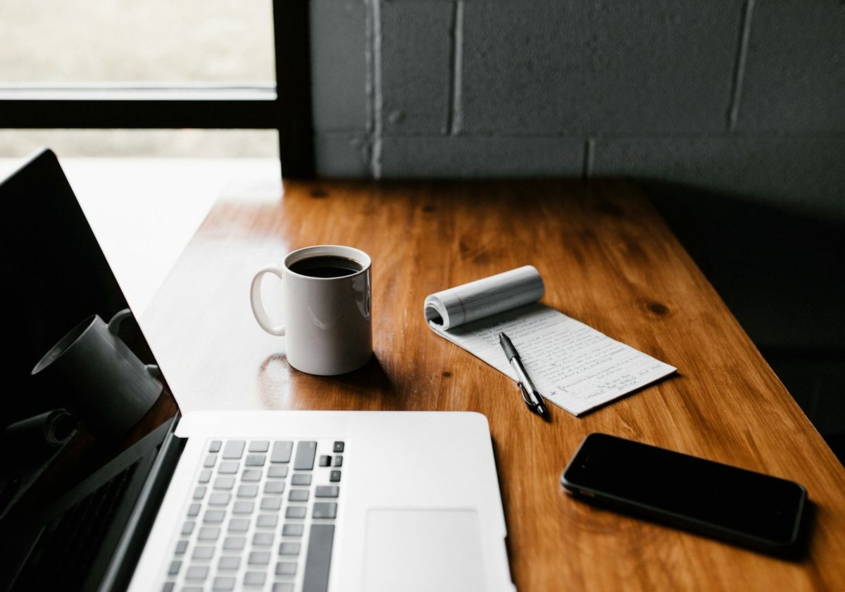 Un bureau avec un ordinateur portable ouvert, un téléphone et une tasse de café