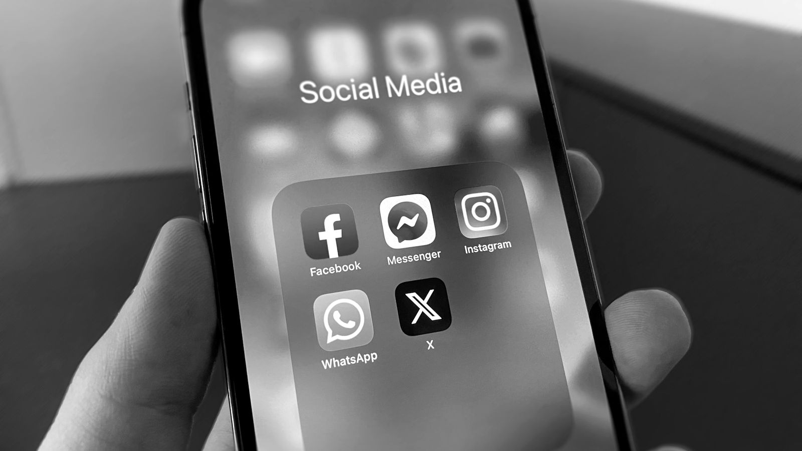 Une main tient un téléphone affichant un dossier d'applications de réseaux sociaux