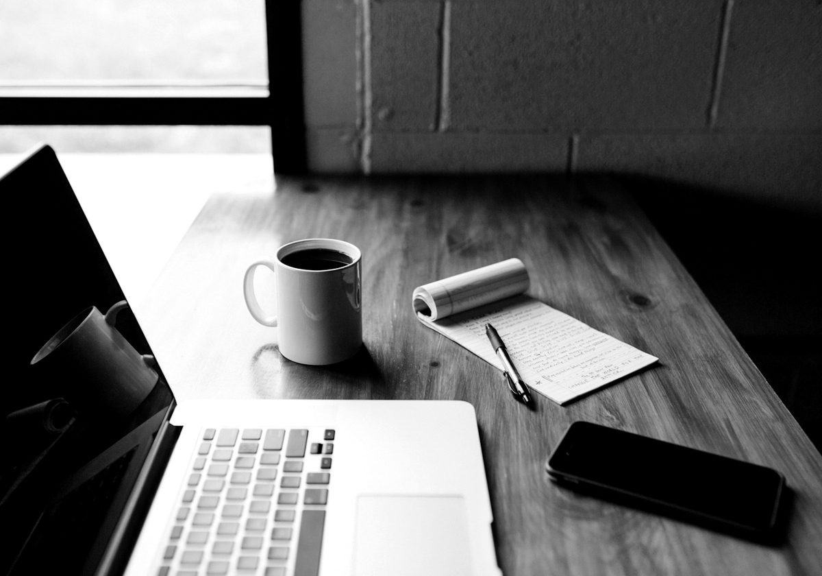 Un ordinateur portable, une tasse de café, un carnet et un téléphone sur un bureau